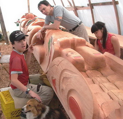 David Neel painting a totem pole with two of his children; Edwin and Ellena