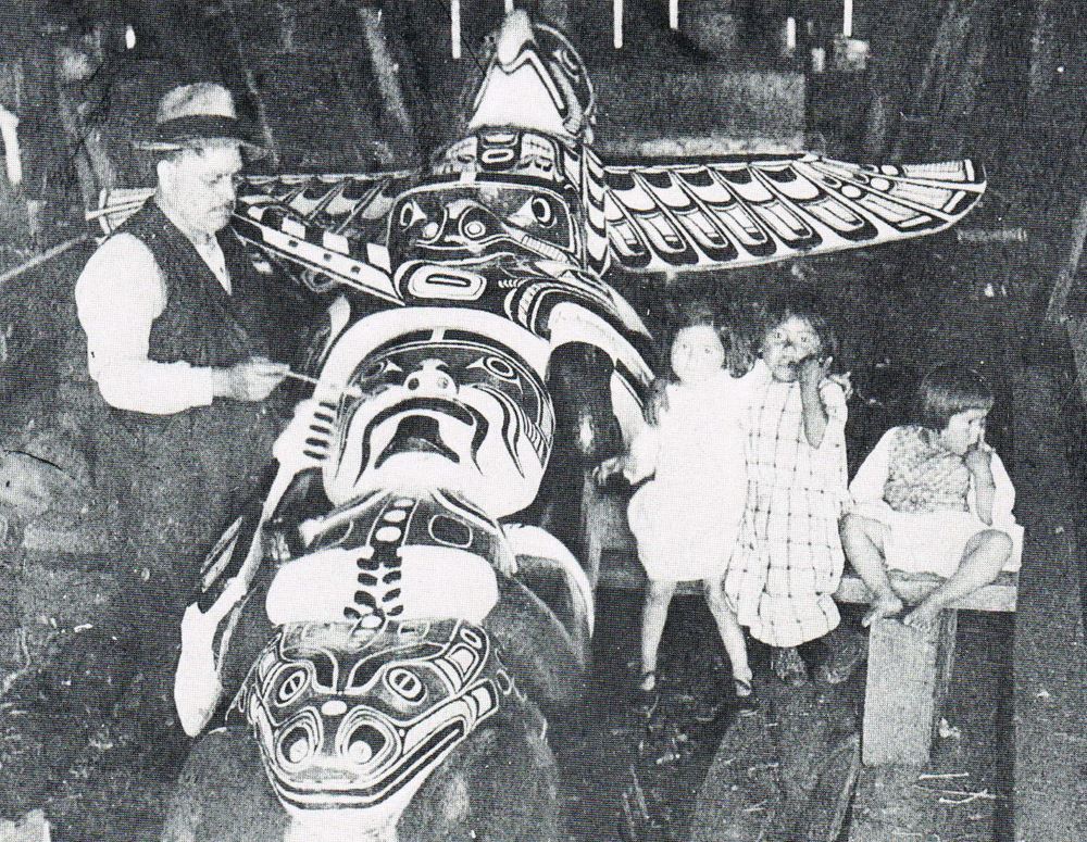 Charlie James carving a totem pole in Alert bay with a young Ellen Neel and her sisters watching.